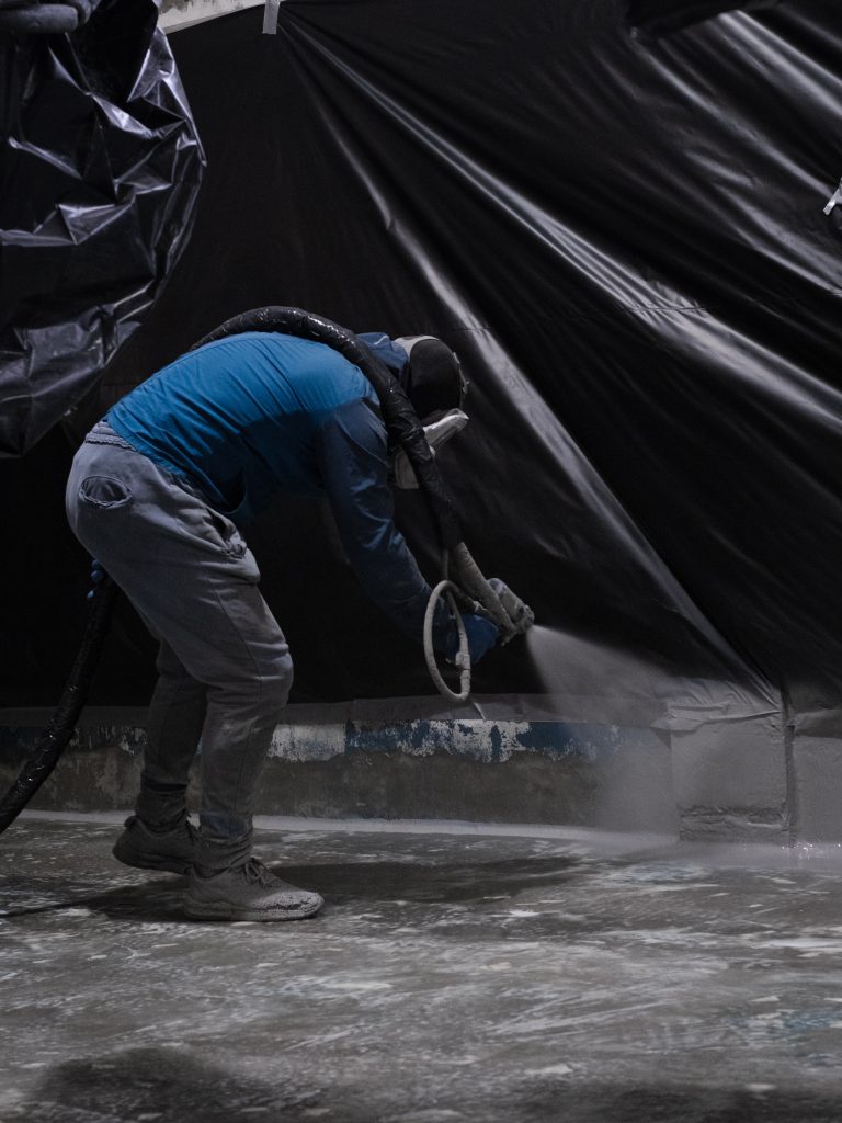 Operador a aplicar poliureia projetada numa instalação industrial